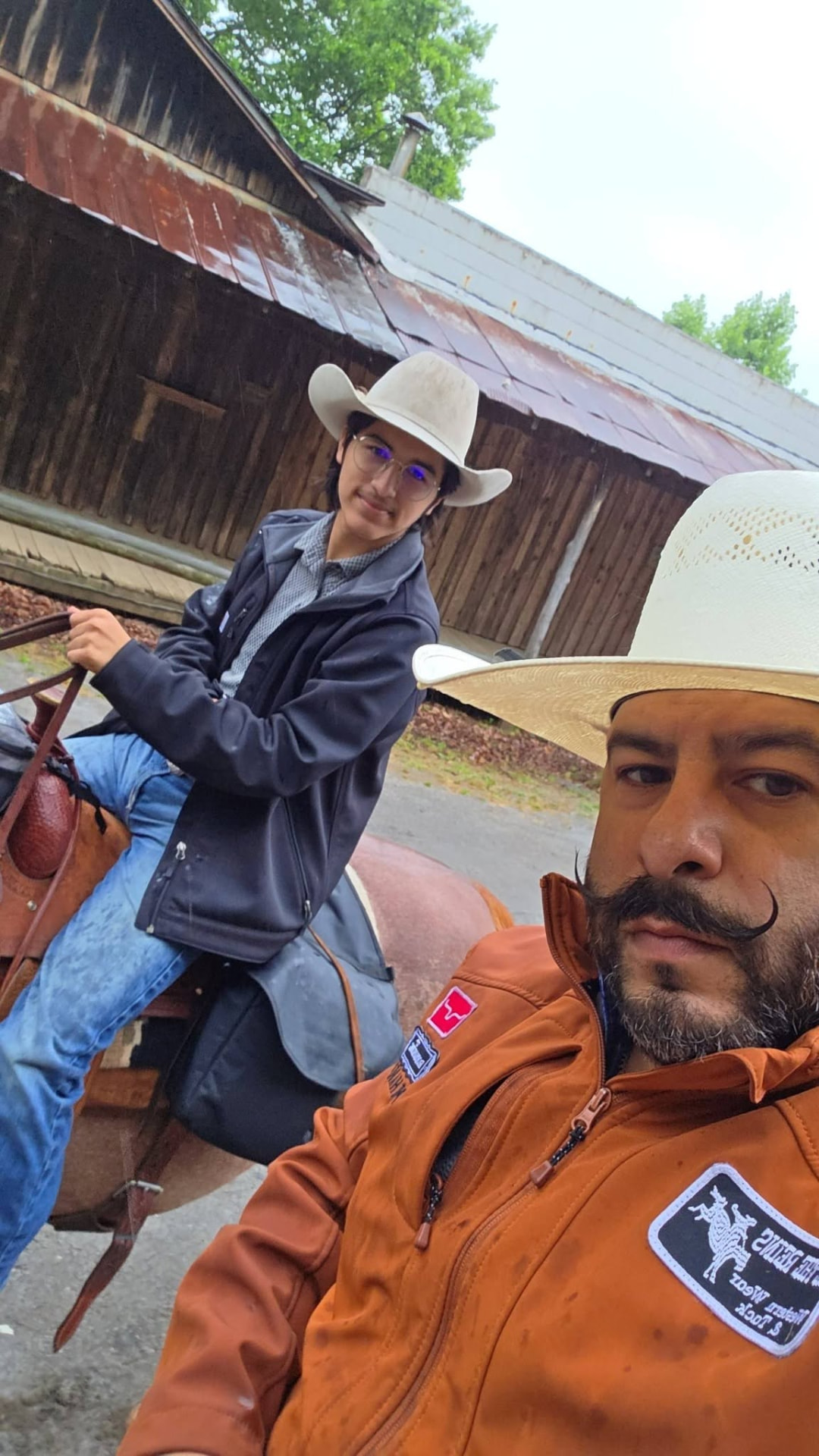 Tex Ruiz and his son Ely with a saddled horse outside an old barn