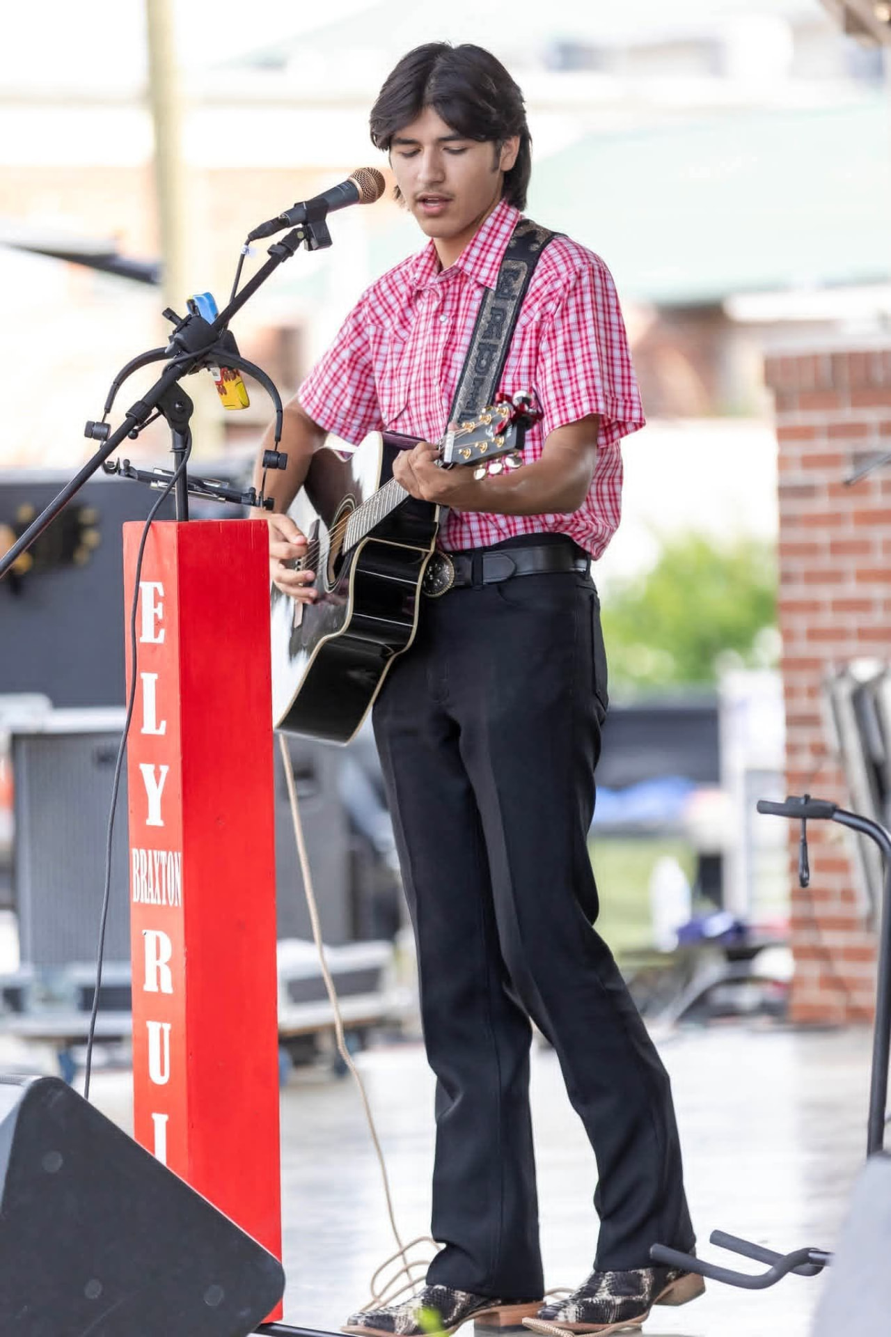 Ely Ruiz playing guitar in a western shirt and boots at a local event